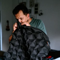 Tata nadmuchuje ustami dmuchaną matę do spania HELP BAG, widać komory powietrzne i logo