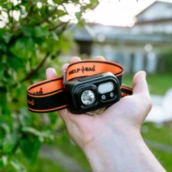 Latarka czołowa USB-C HELP BAG z pomarańczowo-czarną opaską trzymana na dłoni w ogrodzie