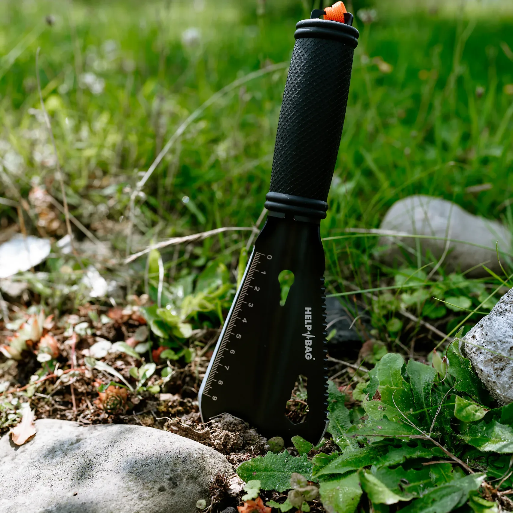 Łopatka stalowa HELP BAG z gumowaną rękojeścią wbita w ziemię między kamieniami w ogrodzie