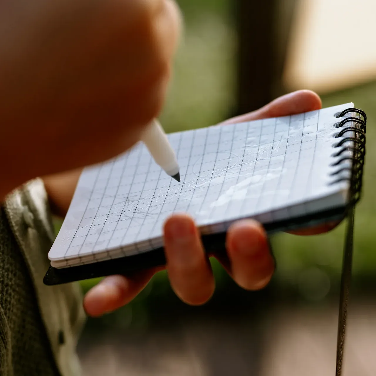 Ołówek pisze po zroszonej wodą kartce w kratkę notesu wodoodpornego HELP BAG