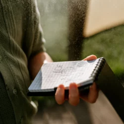 Zapisana kartka w kratkę notesu wodoodpornego HELP BAG trzymana w strudze kropel wody