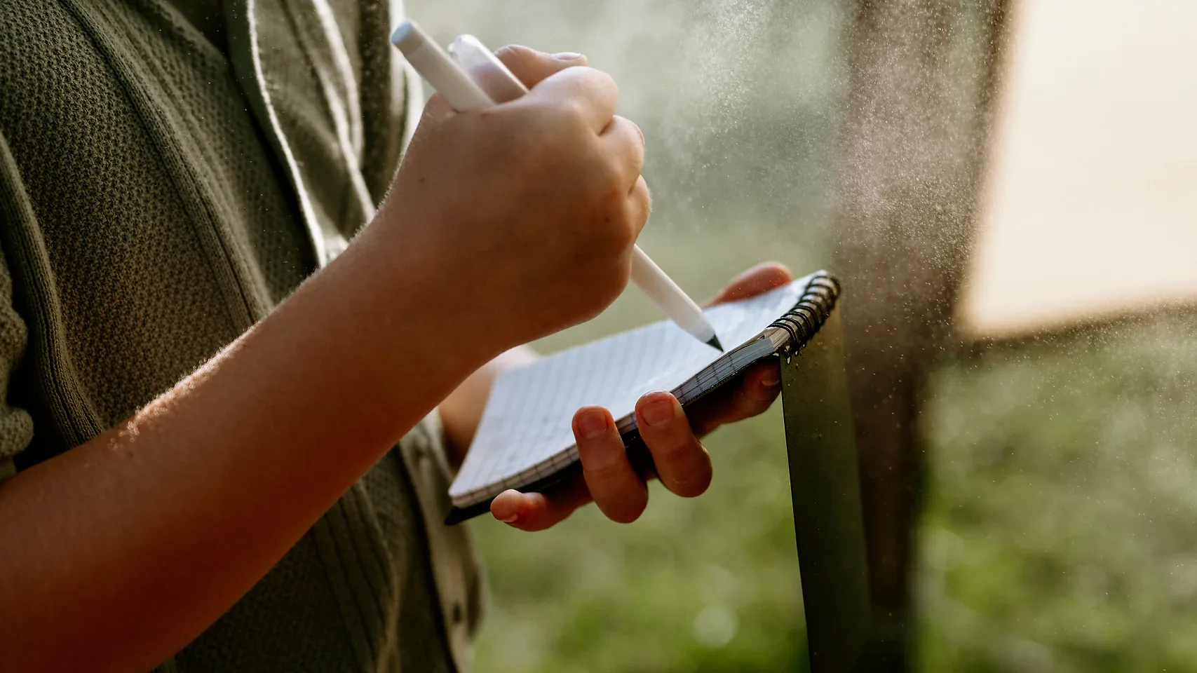 Dziecko pisze ołówkiem w notesie wodoodpornym HELP BAG w mgiełce wody, na zewnątrz