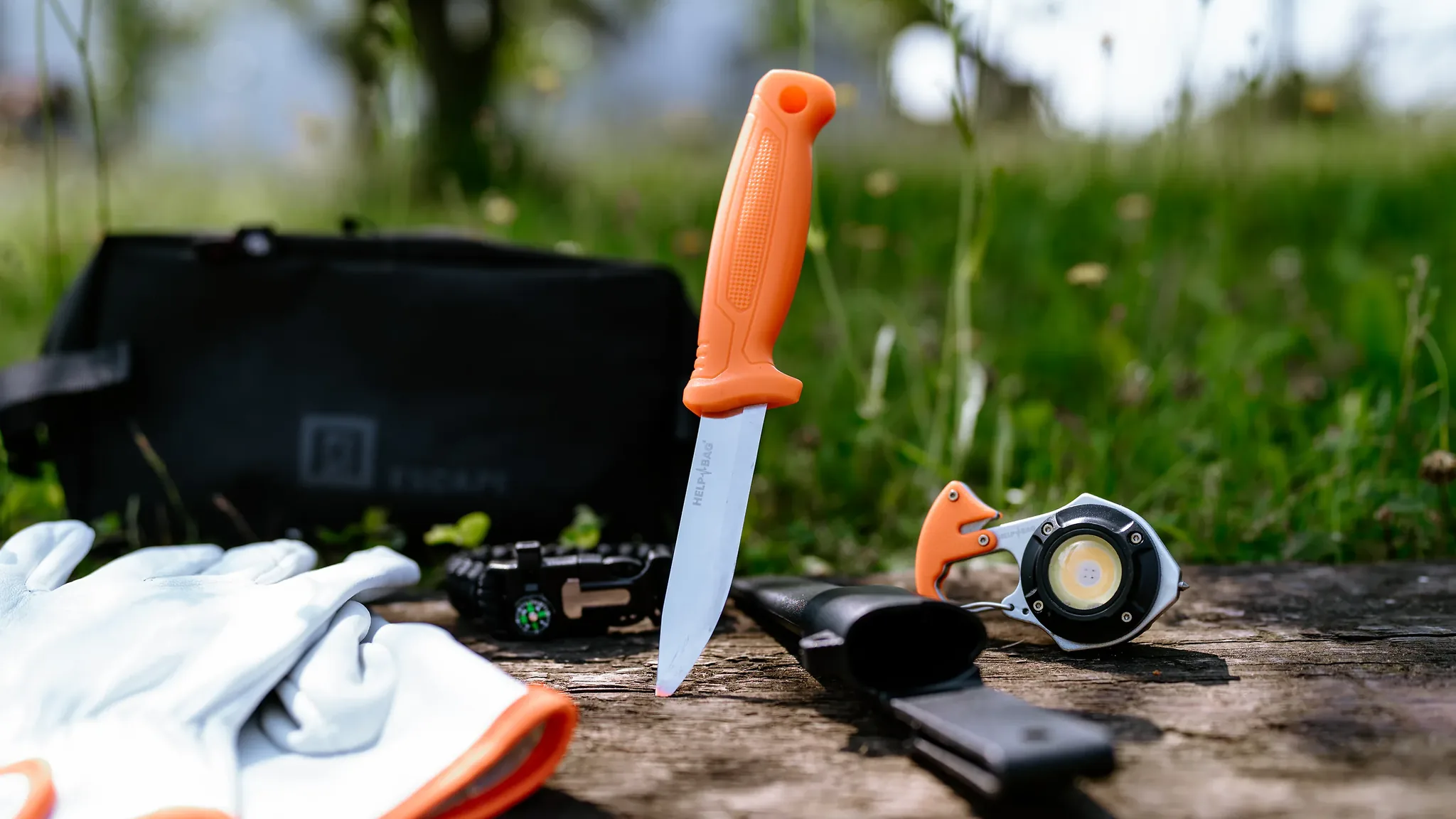 Nóż ze stali nierdzewnej HELP BAG wbity w belkę obok rękawic, bransoletki i torby modułu ESCAPE