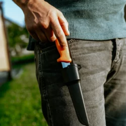 Dłoń wyciąga nóż ze stali nierdzewnej HELP BAG z pomarańczową rękojeścią przy kieszeni spodni