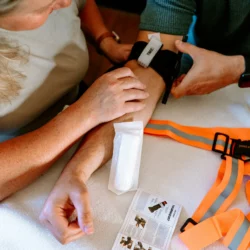 Opaska uciskowa HELP BAG zaciśnięta na ręce tuż pod rękawem, pasek TIME i ulotka z instrukcją