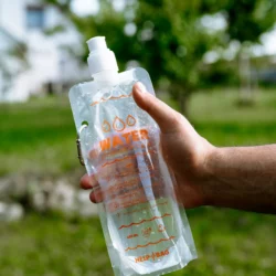 Pełny składany pojemnik na wodę HELP BAG 480 ml w dłoni, widoczny karabińczyk i nadruk WATER