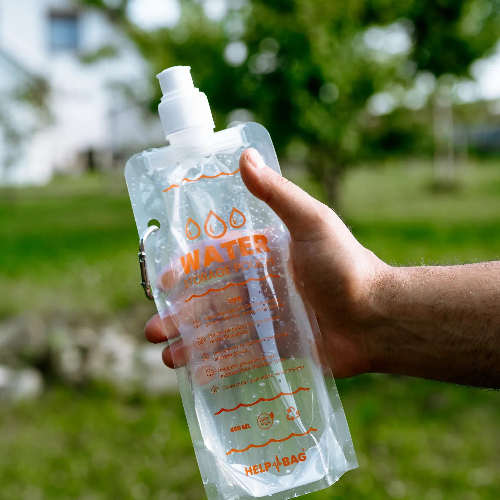 Pełny składany pojemnik na wodę HELP BAG 480 ml w dłoni, widoczny karabińczyk i nadruk WATER