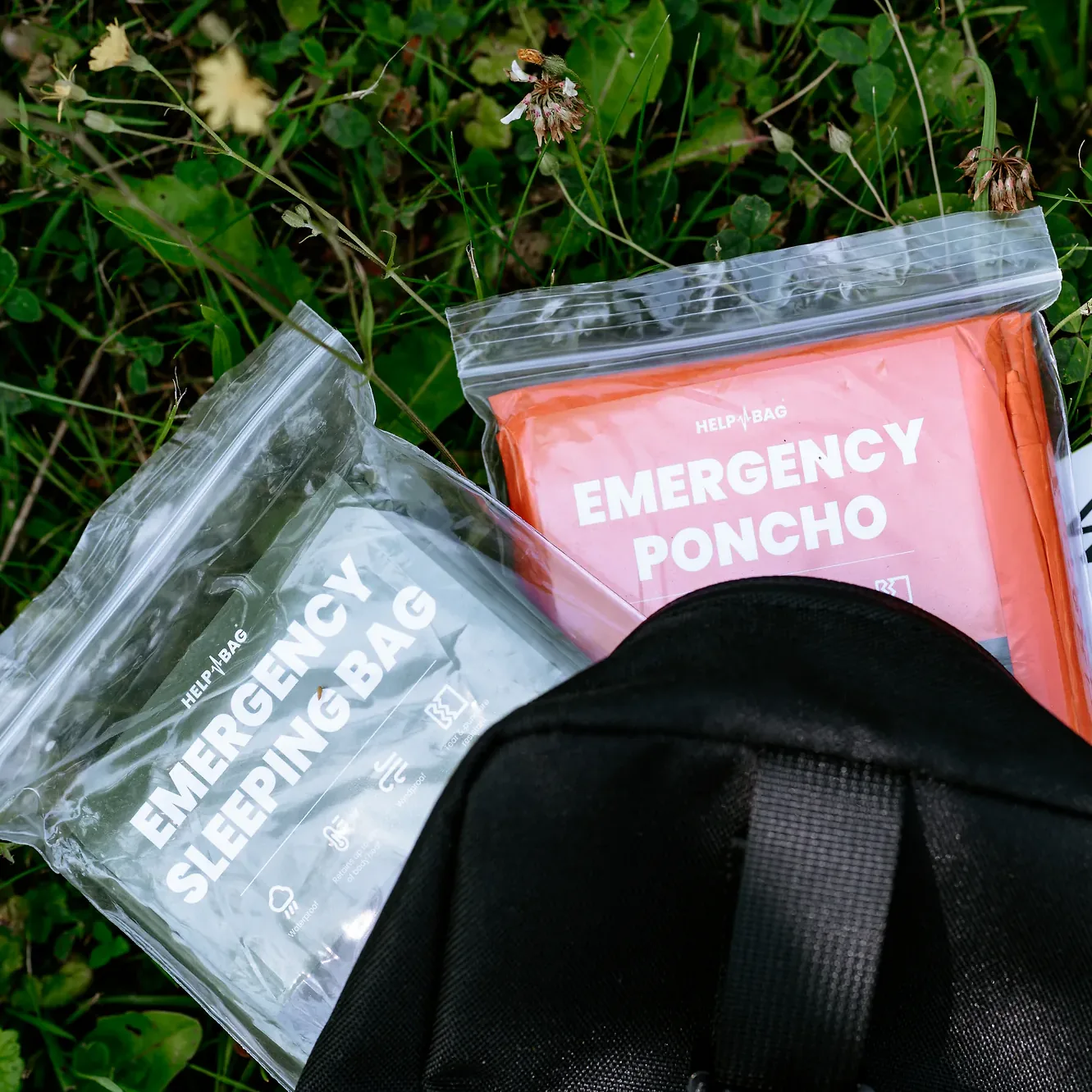 Poncho awaryjne HELP BAG w pomarańczowym opakowaniu EMERGENCY PONCHO obok śpiwora awaryjnego