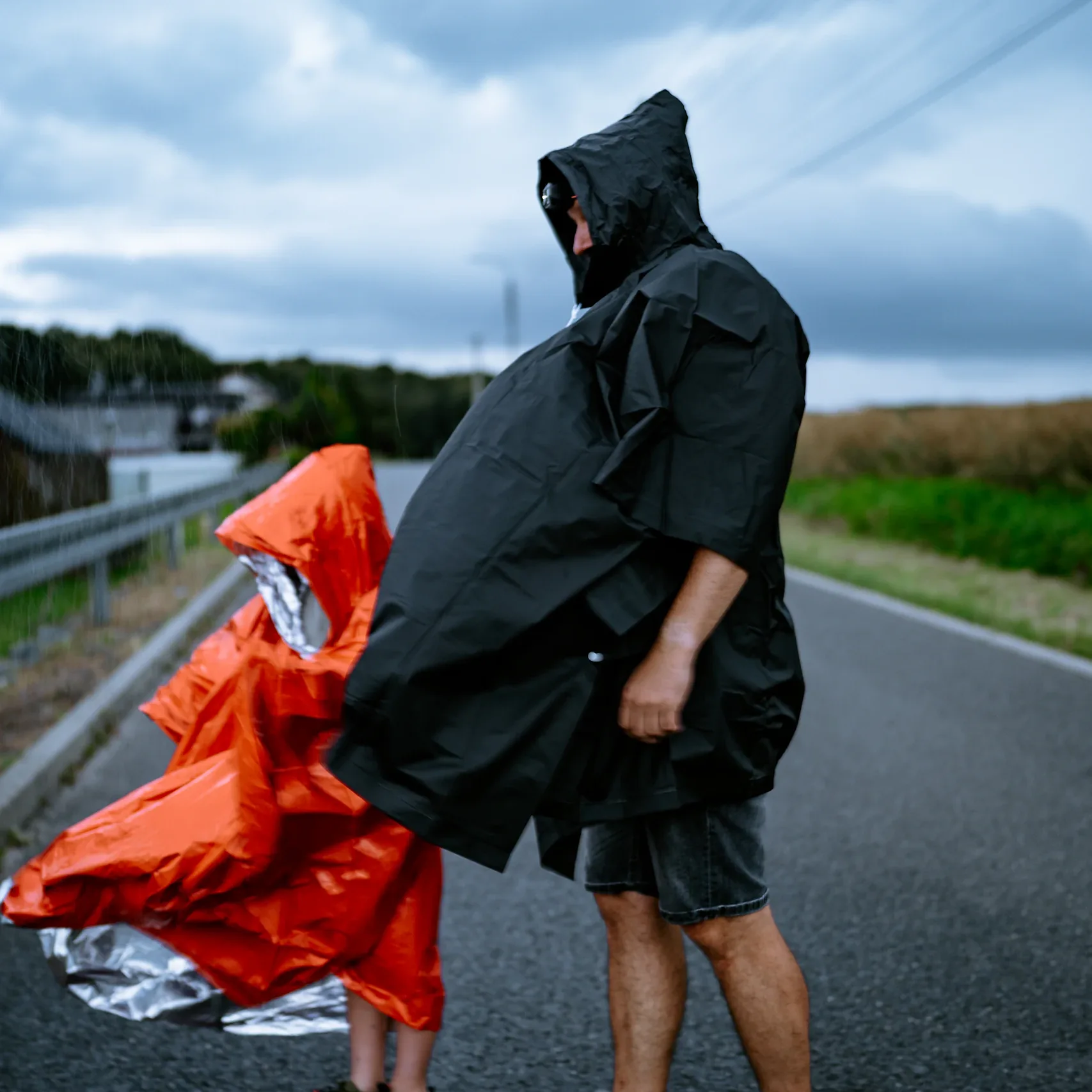 Wiatr rozwiewa czarne poncho przeciwdeszczowe HELP BAG na mężczyźnie stojącym na drodze
