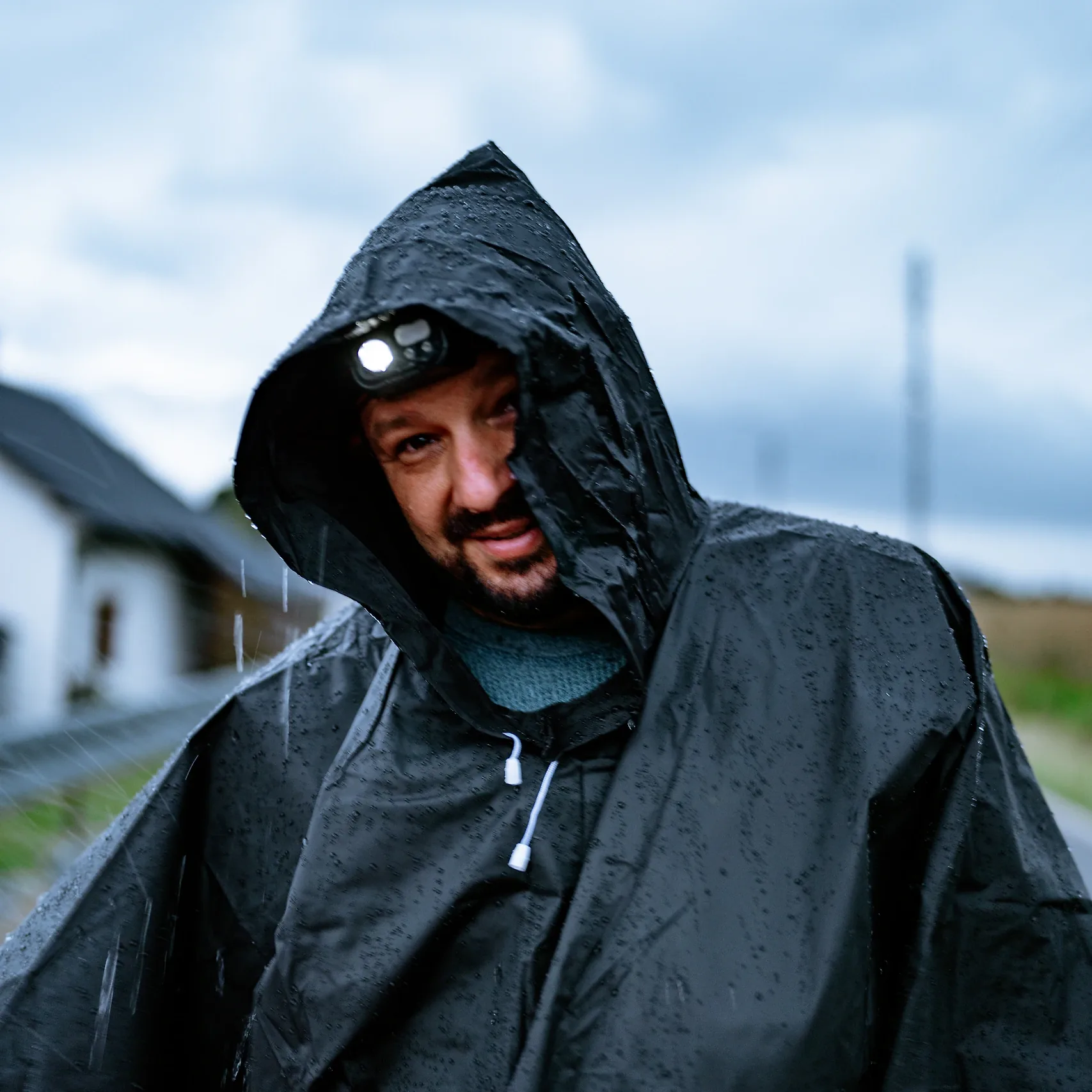 Kaptur i materiał poncho przeciwdeszczowego HELP BAG w kroplach deszczu, pod kapturem latarka czołowa