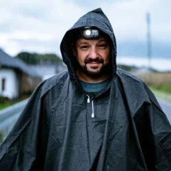 Uśmiechnięty mężczyzna w mokrym poncho przeciwdeszczowym HELP BAG z kapturem i latarką czołową