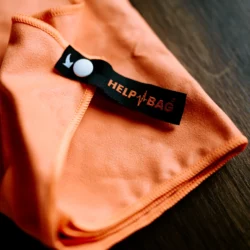 Metka HELP BAG z zatrzaskiem na pomarańczowym ręczniku z mikrofibry, widać obszycie brzegu