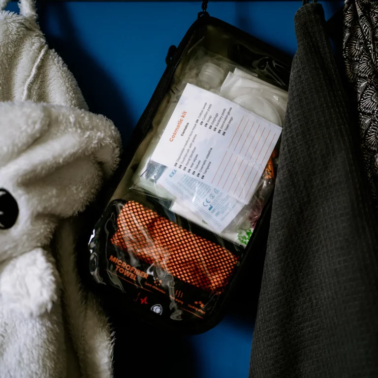 Аварійний комплект HELP BAG MAX PRO Moduł HYGIENE HELP BAG z ręcznikiem z mikrofibry i kosmetyczką zawieszony na wieszaku obok szlafroków