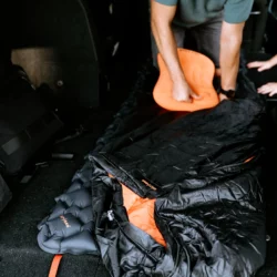 Tata rozkłada w aucie śpiwór HELP BAG na dmuchanej macie i kładzie na nim pomarańczową poduszkę
