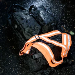 Szelki odblaskowe HELP BAG na mokrym plecaku nocą, pasy ostrzegawcze odbijają światło latarki
