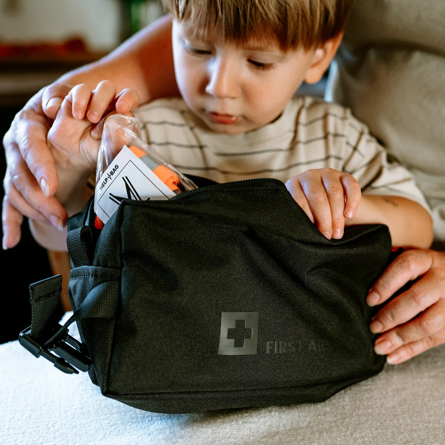 Dziecko z pomocą mamy pakuje szelki odblaskowe HELP BAG w woreczku do modułu FIRST AID