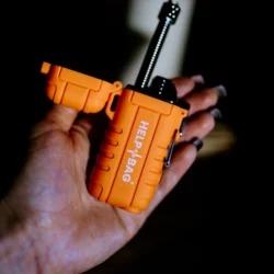 Otwarta zapalniczka plazmowa HELP BAG z wysuniętym wężykiem w dłoni, w tle zapalone świece