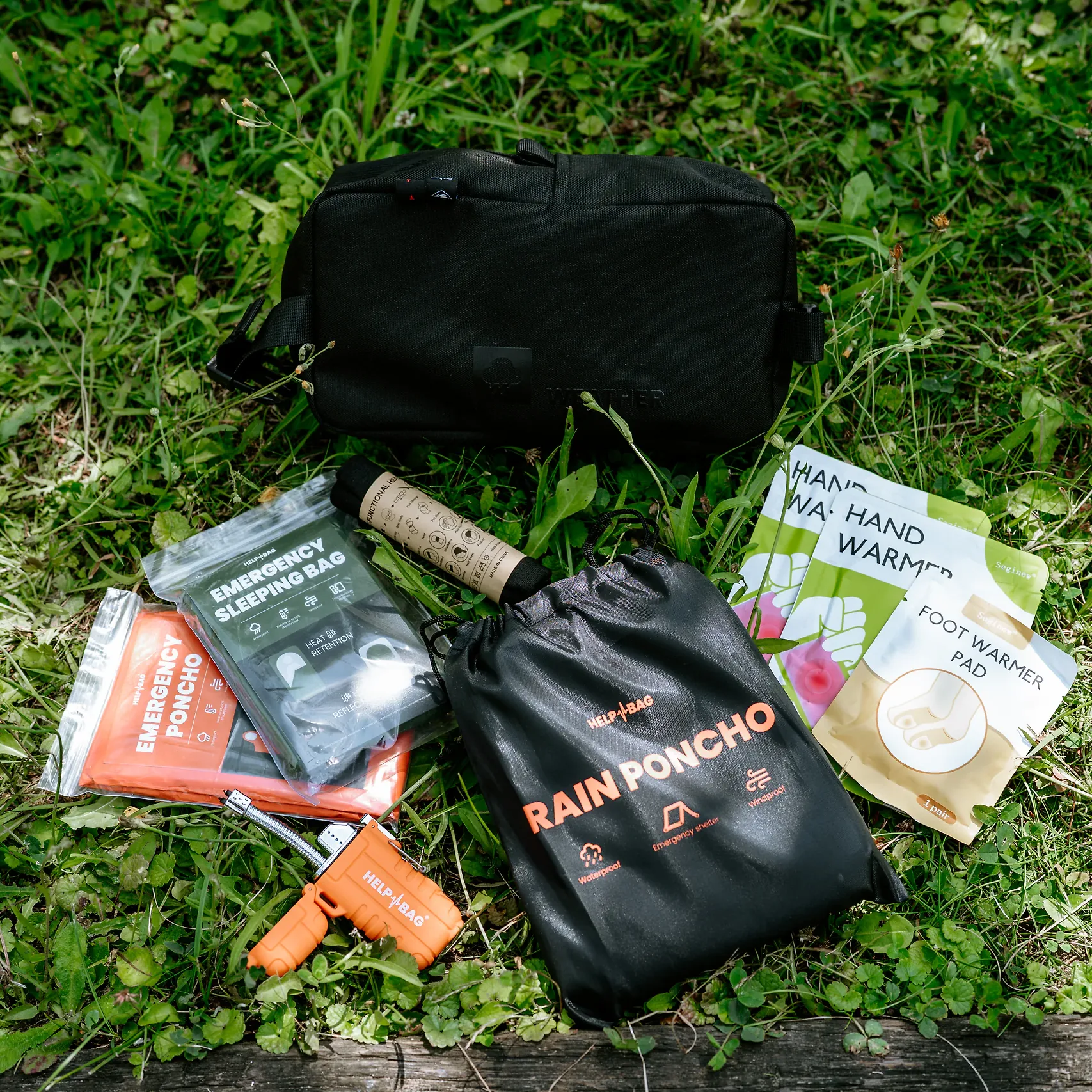Zapalniczka plazmowa HELP BAG na trawie przed modułem WEATHER, obok śpiwora awaryjnego i ogrzewaczy