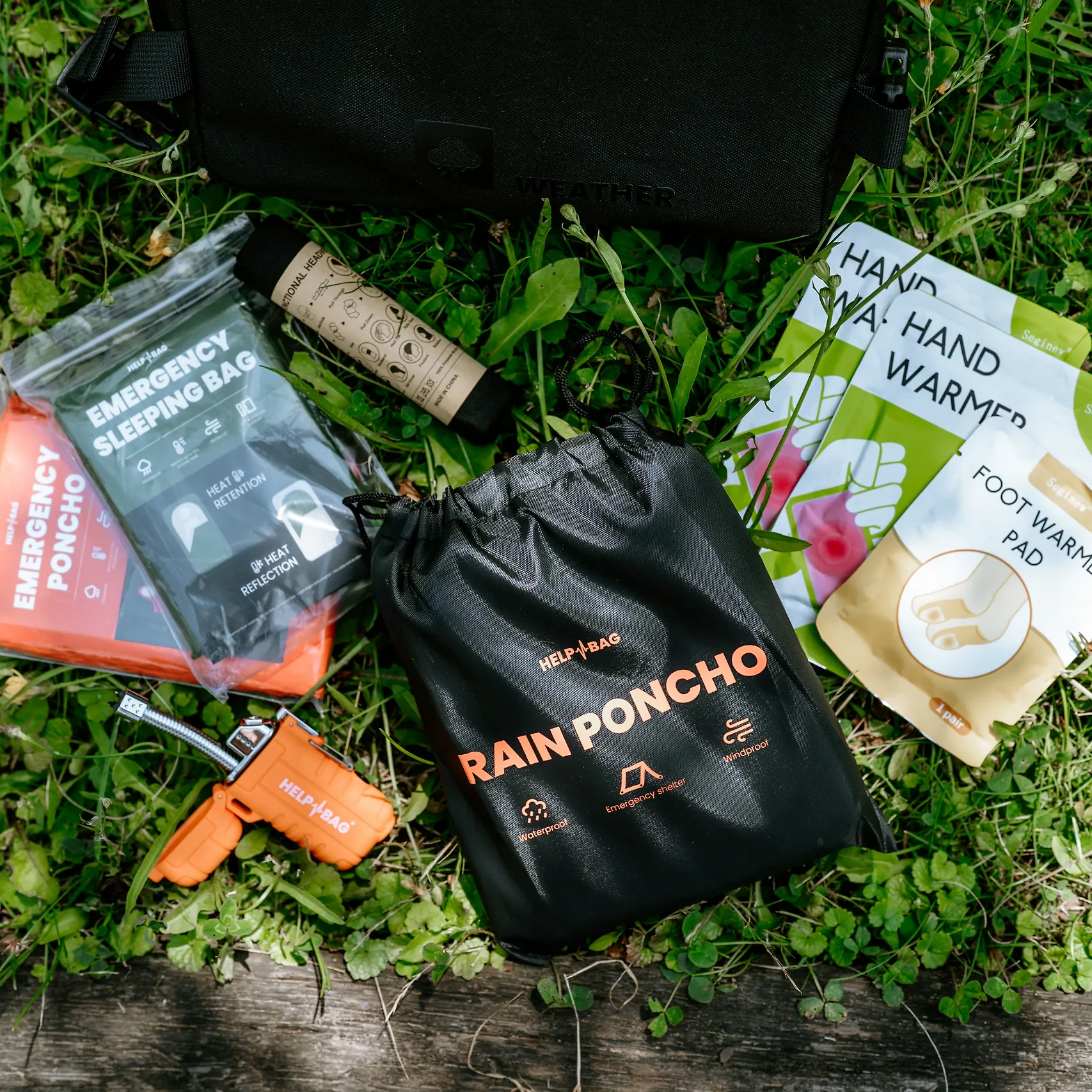 Zawartość modułu WEATHER HELP BAG na trawie: śpiwór awaryjny, poncho, ogrzewacze i zapalniczka plazmowa
