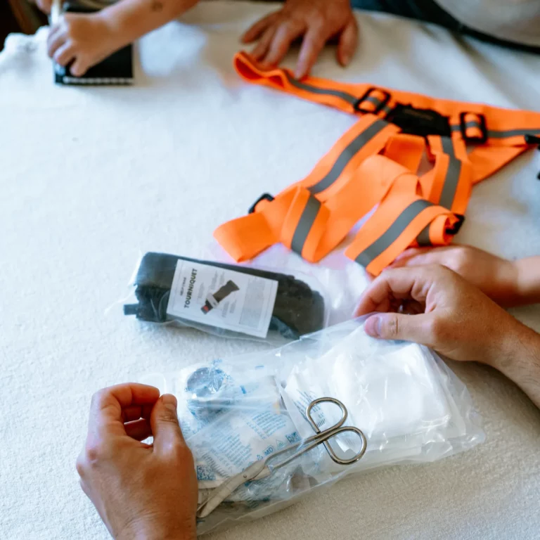 Аварійний комплект HELP BAG MAX PRO Fabrycznie zapakowana opaska uciskowa HELP BAG obok szelek odblaskowych i opatrunków