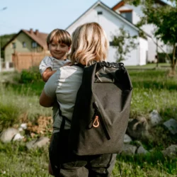 Mama niesie dziecko na ręku, na plecach ma zestaw awaryjny HELP BAG BASIC w wodoodpornym plecaku